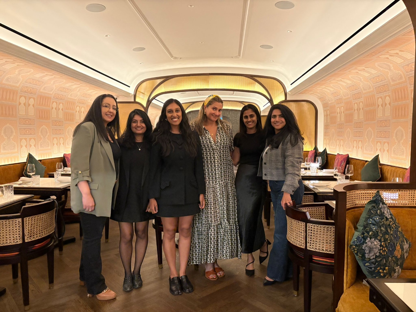 Six South Asian women gathered for a curated Desi Dinner in a warm, Mughal-inspired restaurant