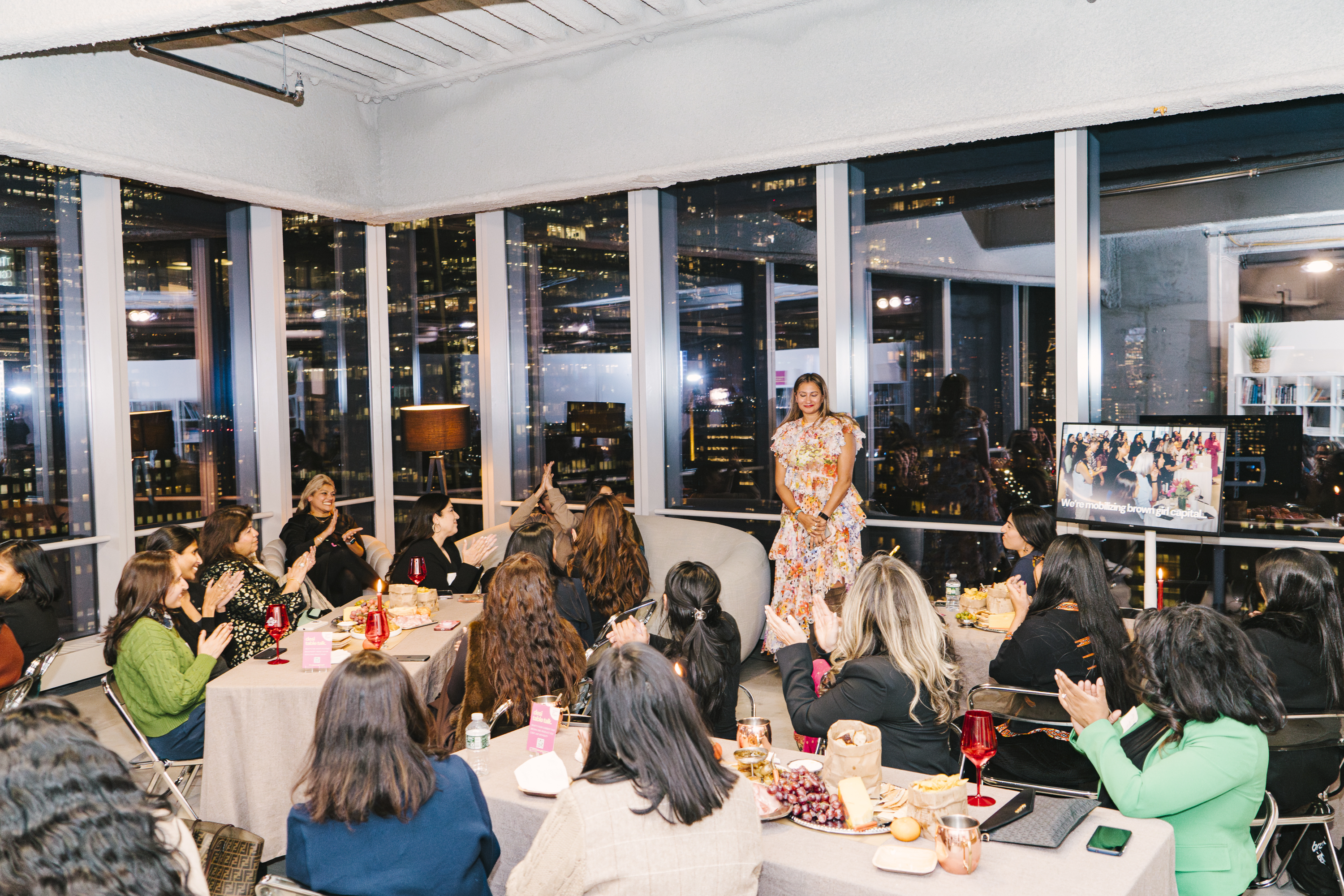 Bhargavi Varma speaking to a room of senior South Asian women at the SickKids fundraiser — 'We're mobilizing brown girl capital' on screen.